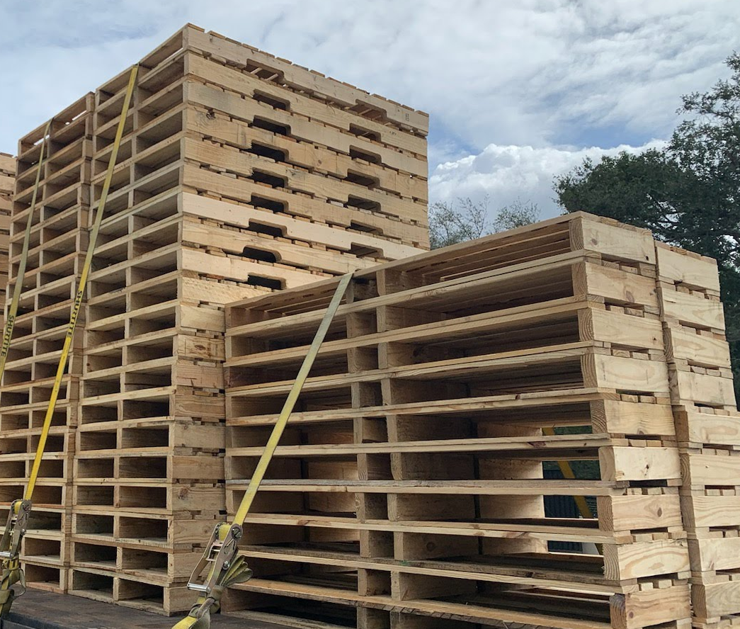Stacked wooden pallets and large shipping crates outdoors in a yard under a cloudy sky