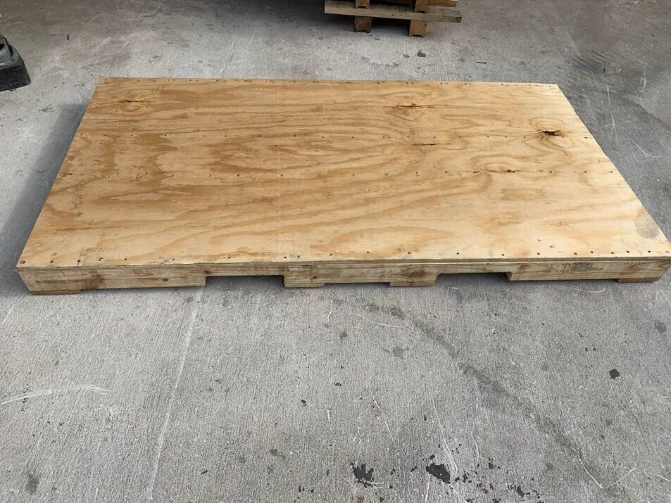 Large plywood sheet resting on a wooden pallet on a concrete floor.