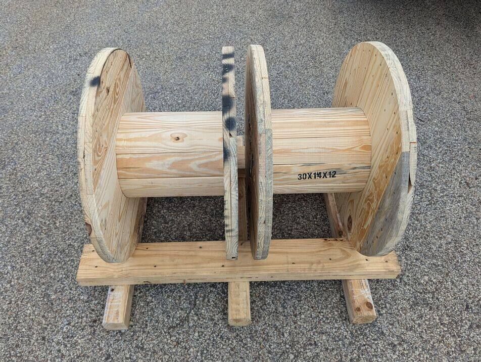 Wooden cable reel on a pallet, viewed from the side on gravel.