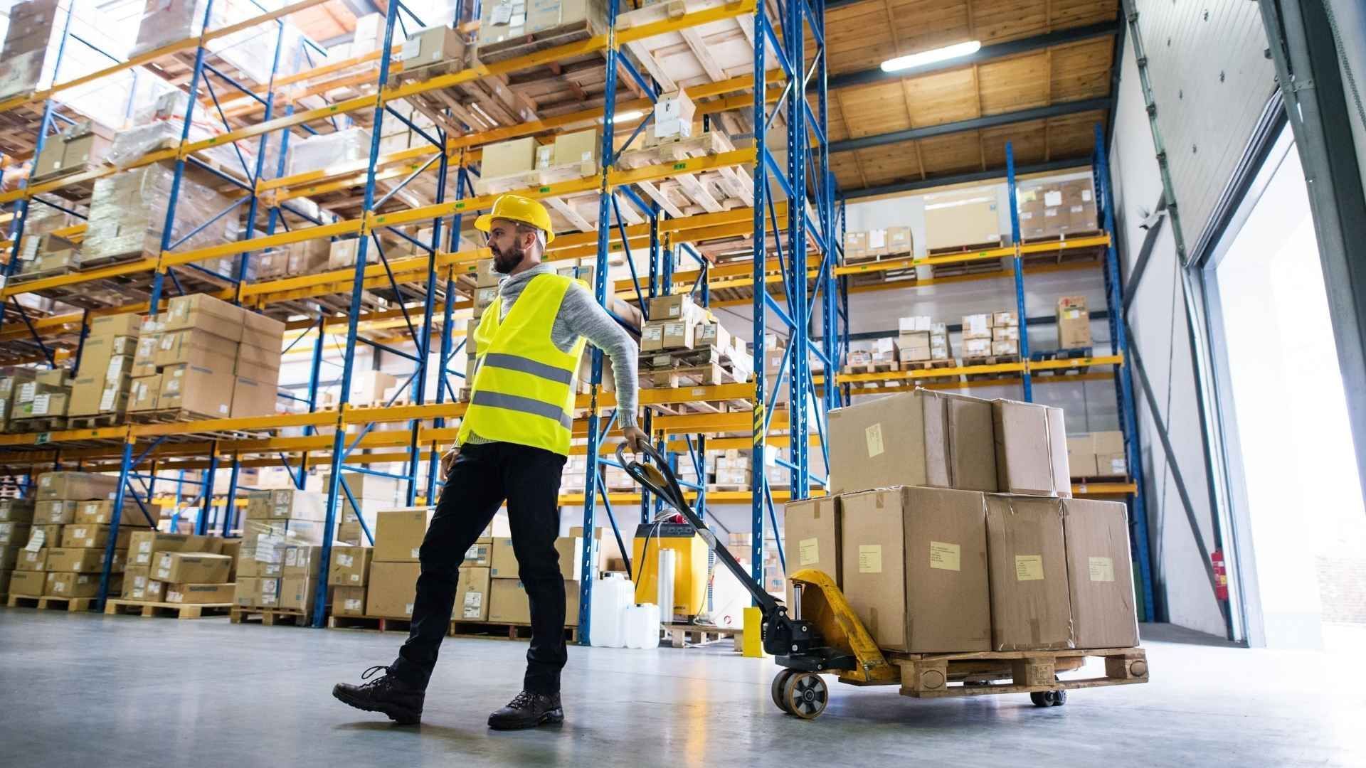 A man is pushing a pallet with boxes on it in a warehouse.