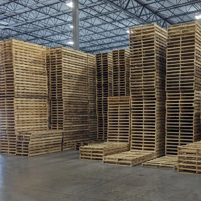 Stacks of empty wooden pallets in a large warehouse with a metal truss ceiling.