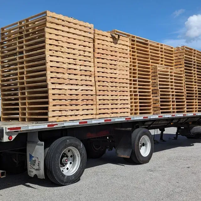 Flatbed trailer loaded with stacked wooden pallets on a sunny lot.