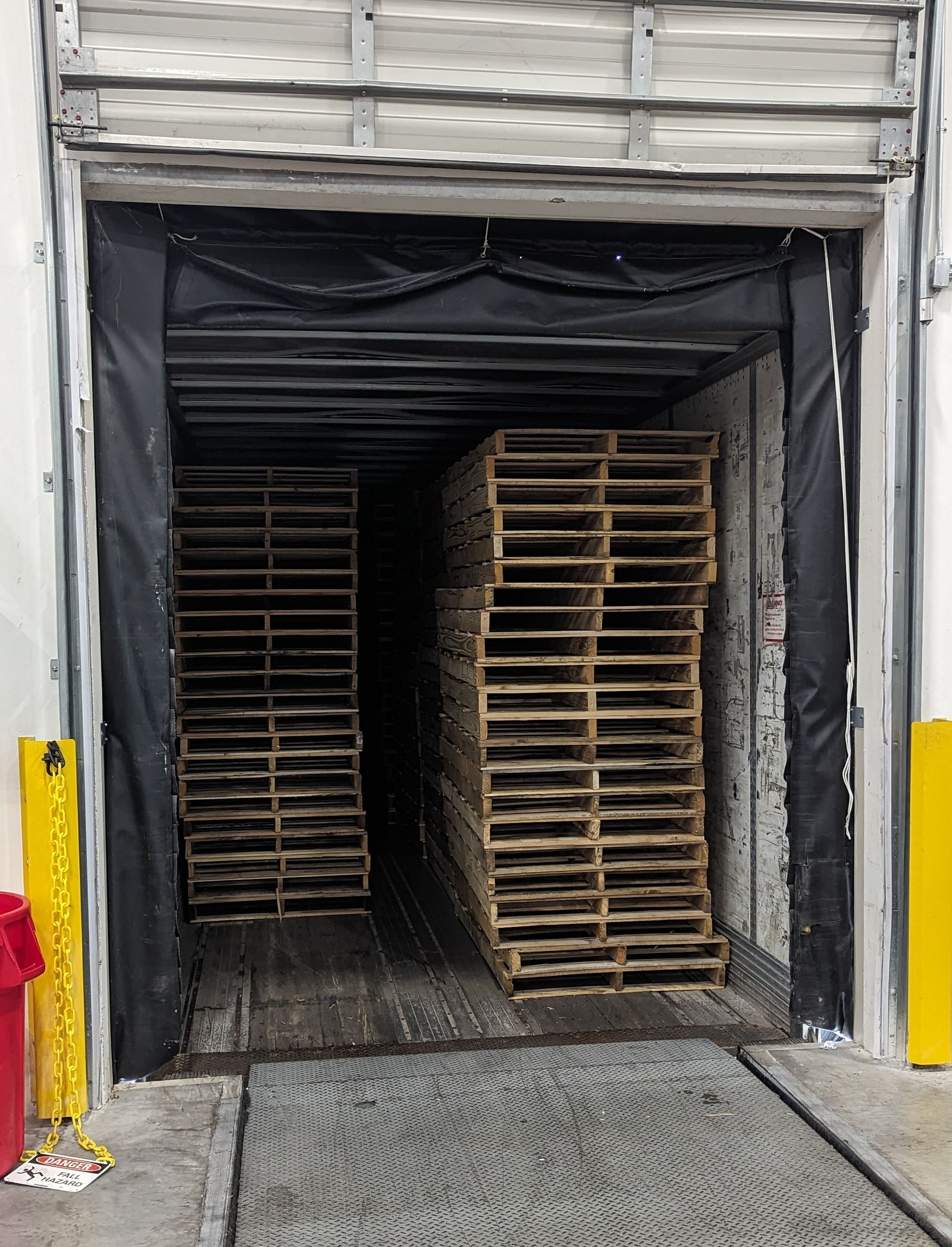Open rear of a cargo truck loaded with stacked wooden pallets at a wet loading area