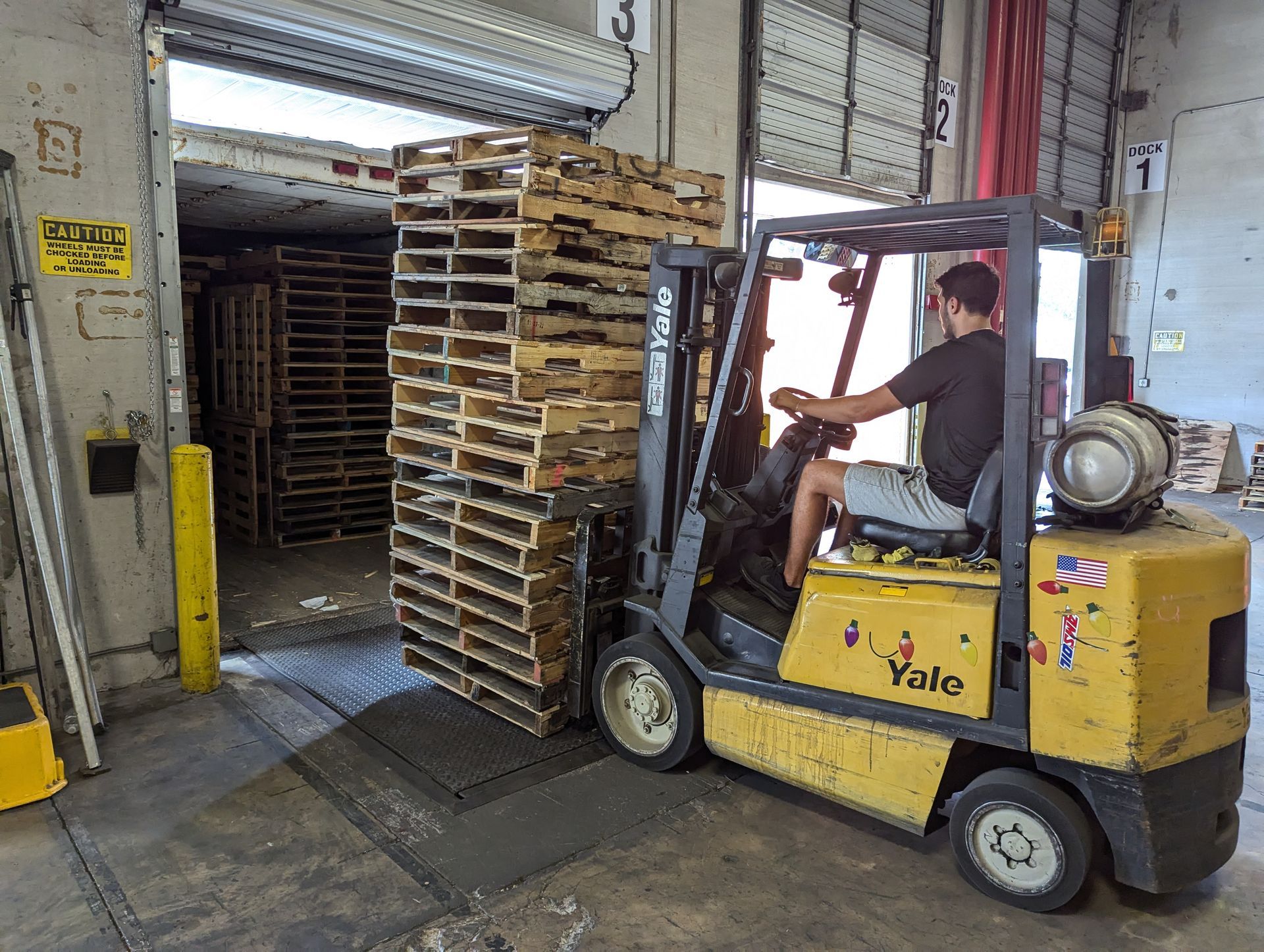 White flatbed truck loaded with stacked wooden pallets parked outdoors on a sunny street