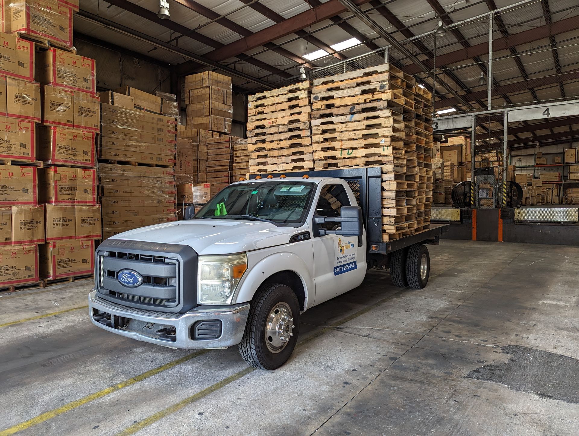 White delivery truck loaded with stacked wooden pallets in an industrial lot under a blue sky