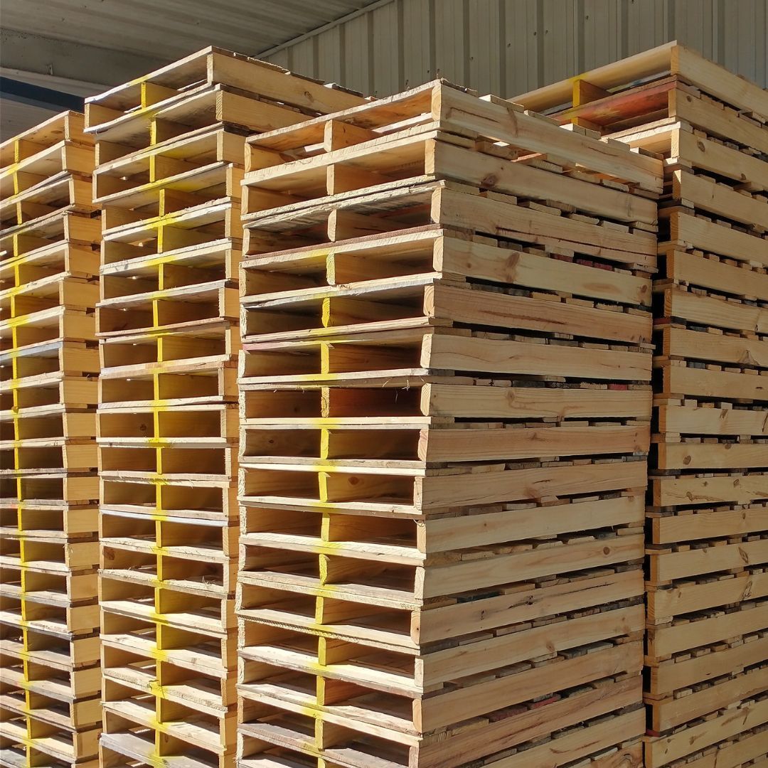 Stacks of wooden pallets in a warehouse, with yellow separators visible between the slats.