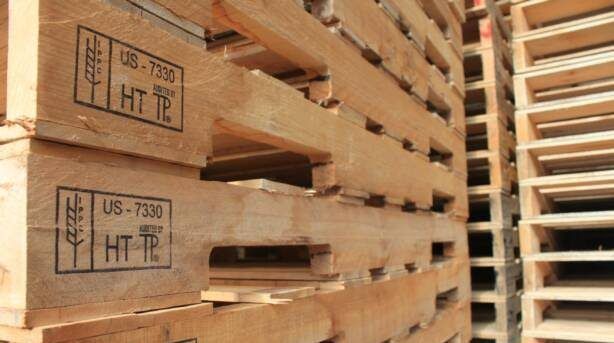 Stacks of wooden pallets in a warehouse, with stamped markings on the side.