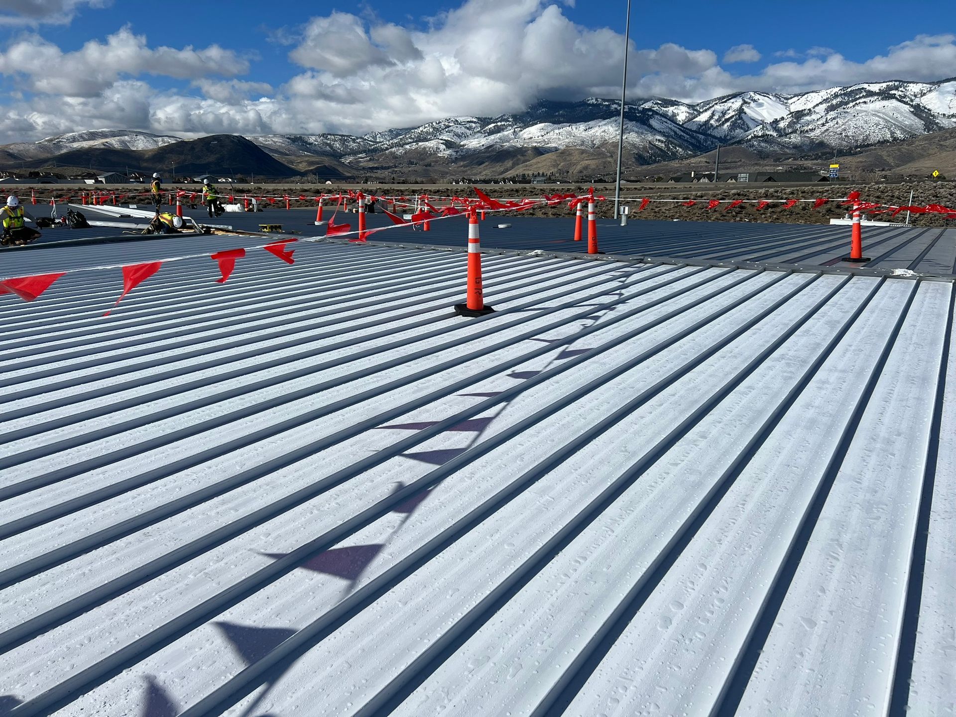 Corrugated metal roof partially covered in snow; mountains in the background, topped with snow. 