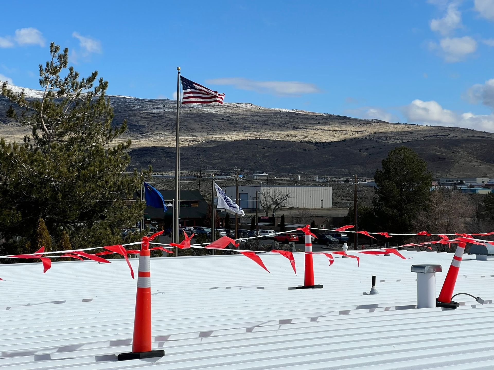 Rooftop with orange cones, flags, and a distant mountain under a blue sky.
