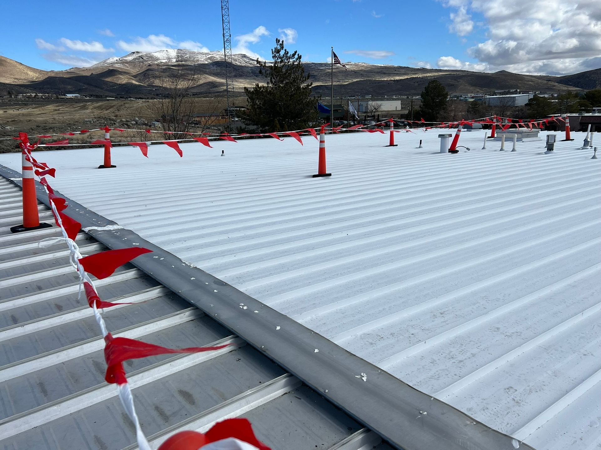 White-coated corrugated metal roof with orange cones and red flags; mountains in the background.