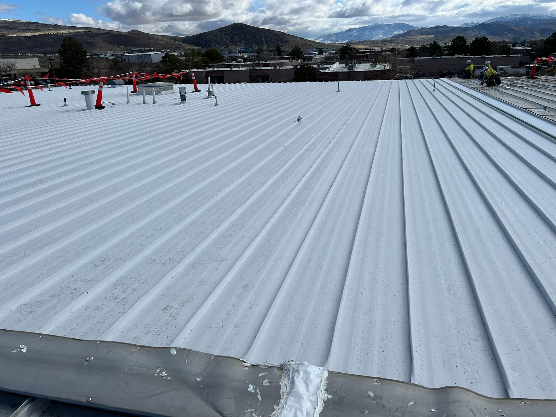 White corrugated metal roof under a bright sky. Workers in vests on the right side.