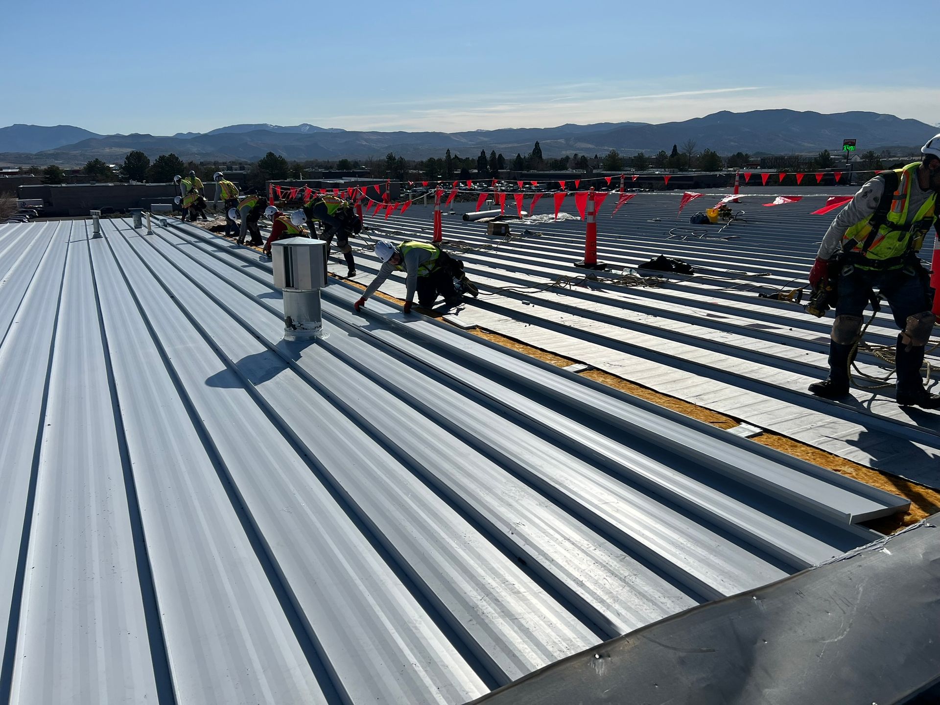 Construction workers installing a metal roof on a building; safety harnesses and equipment visible.