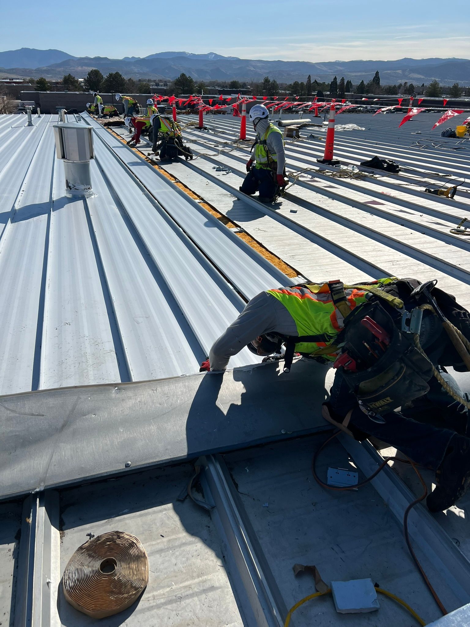 Construction workers on a metal roof, wearing safety vests and helmets. 