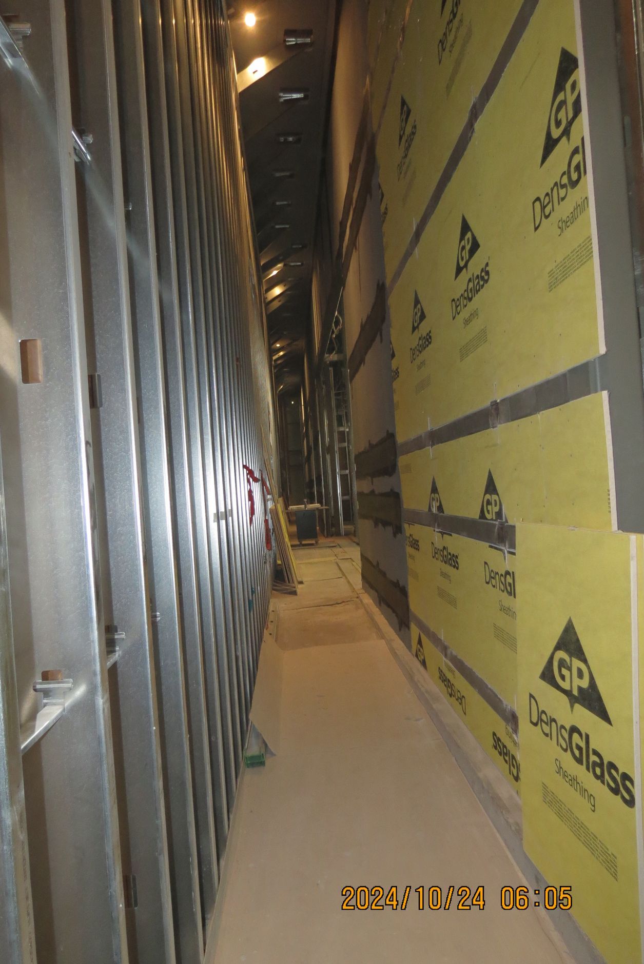 Narrow construction hallway with metal studs on the left and insulated wallboard on the right.