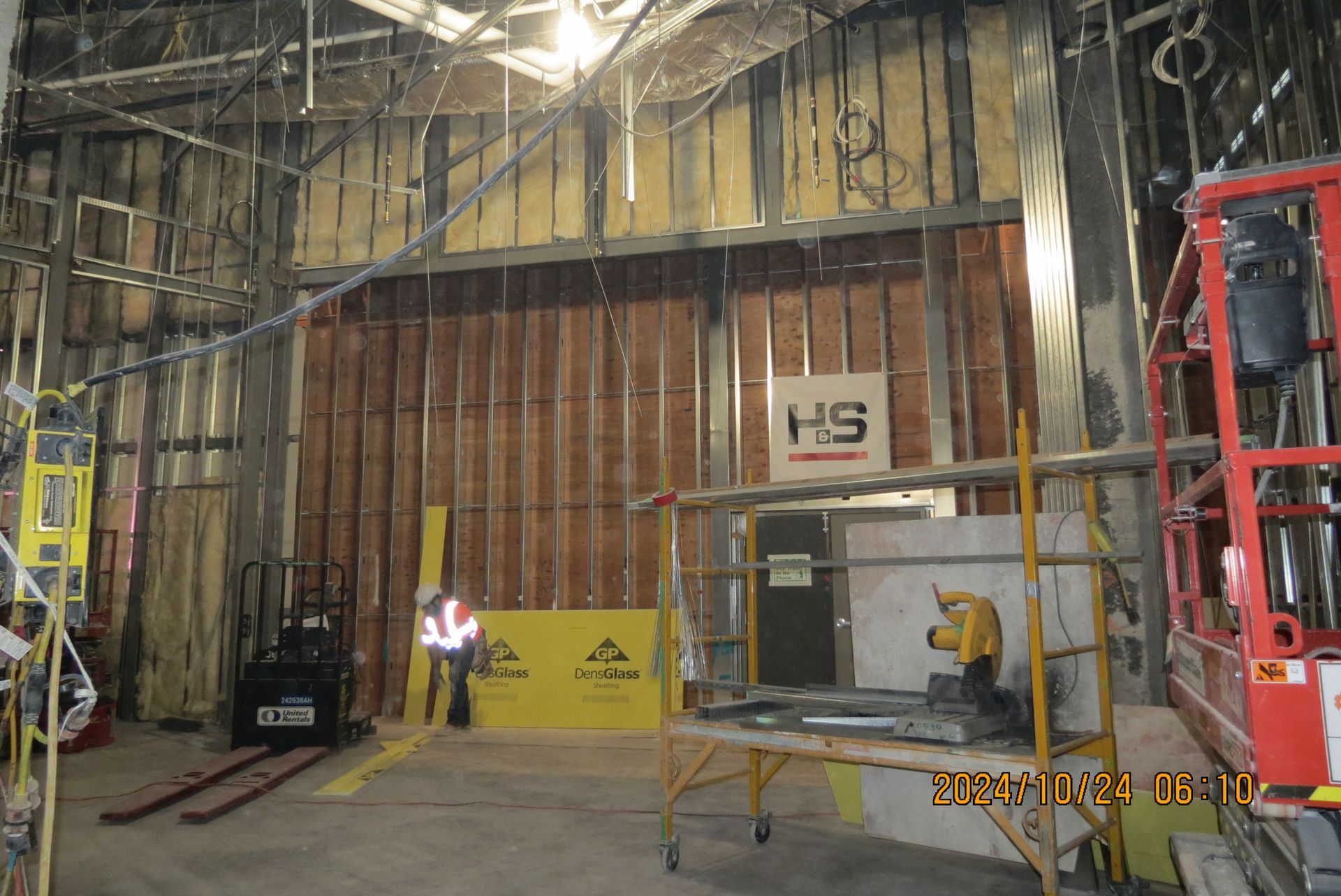 Construction site interior: framing, insulation, a person in a vest, a forklift, and equipment.
