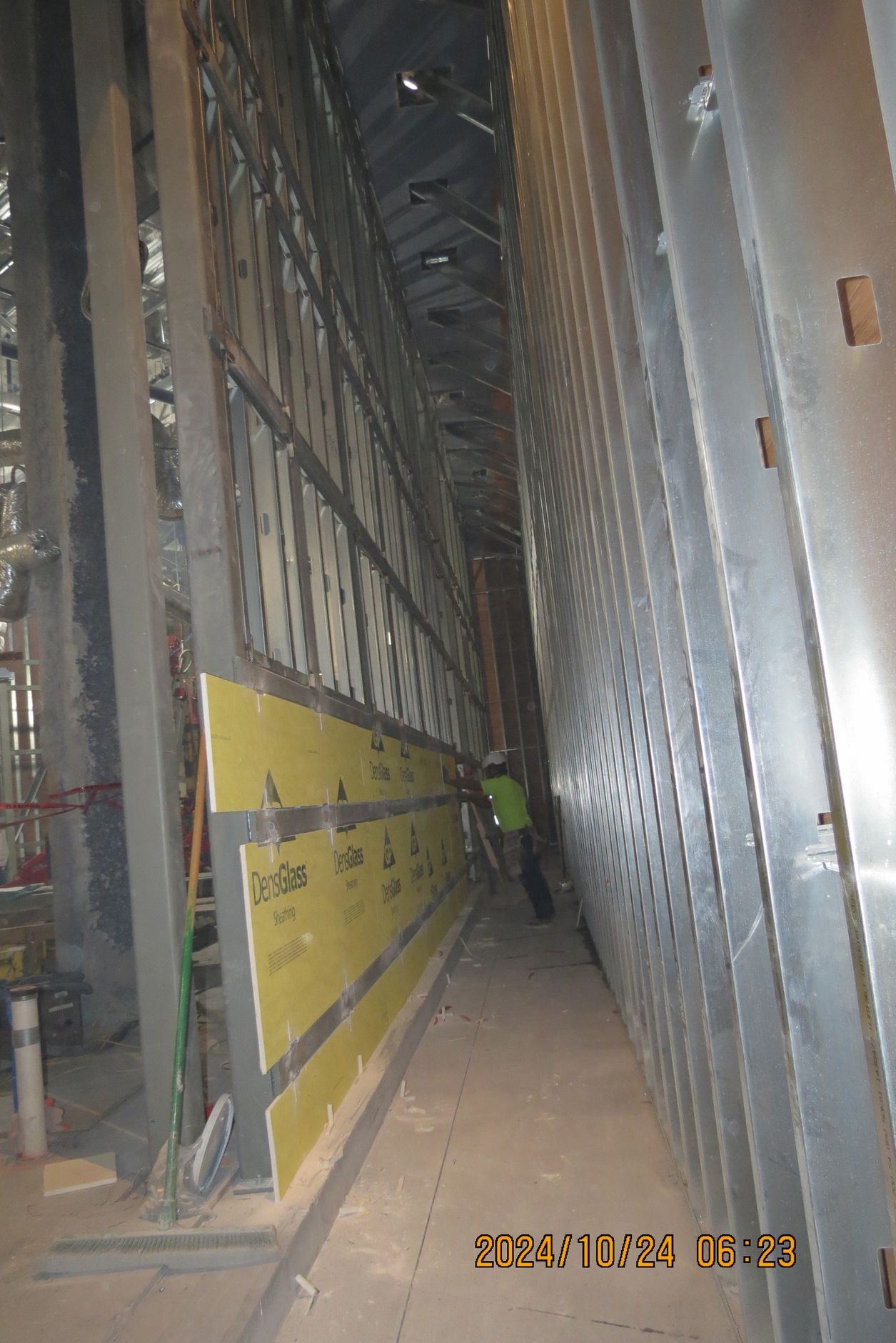 Construction site interior with metal framing and yellow panels. Worker in green safety vest.