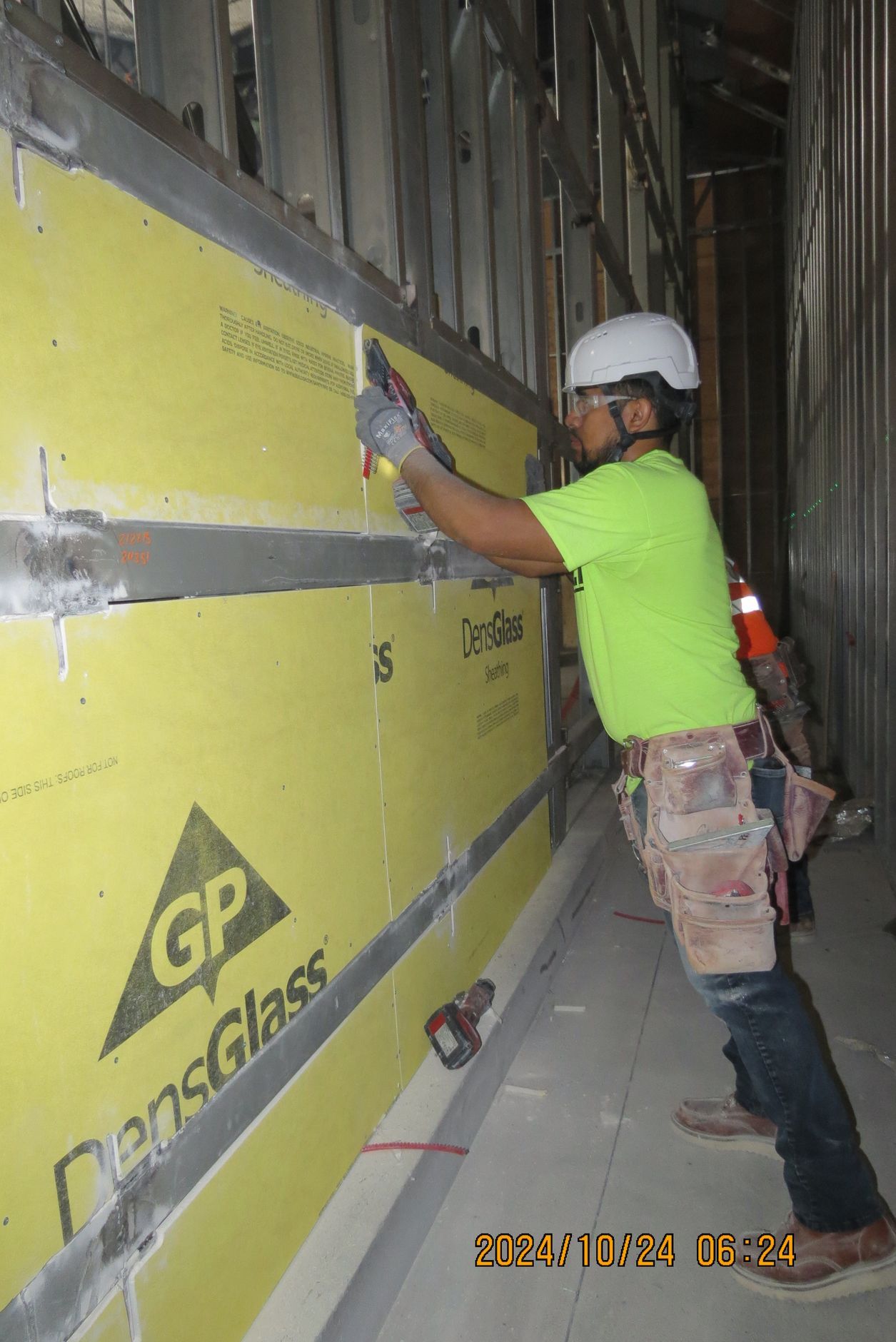 Construction worker applying compound to yellow DensGlass wall panels.