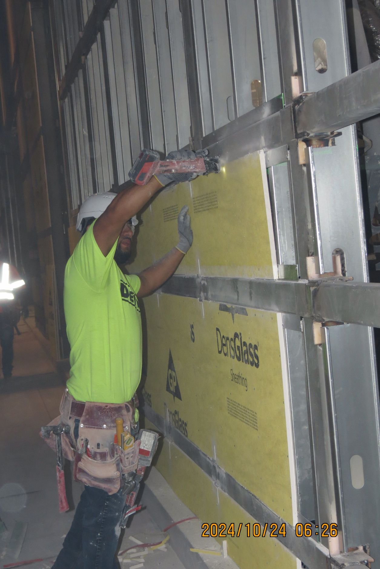 Construction worker installing wall panels using a power tool on a construction site.