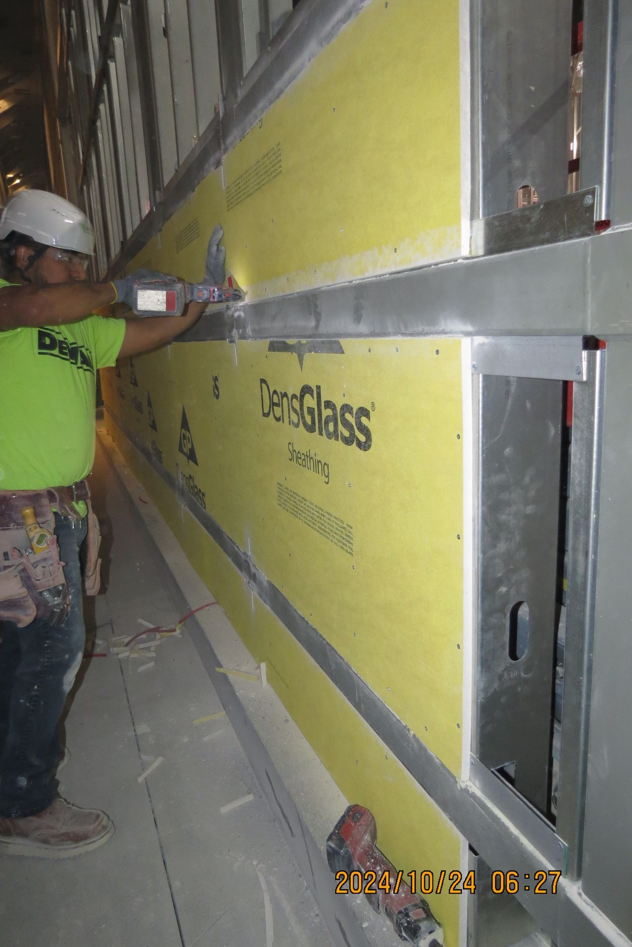 Construction worker using a tool to attach yellow DexGlass paneling to a metal wall frame.
