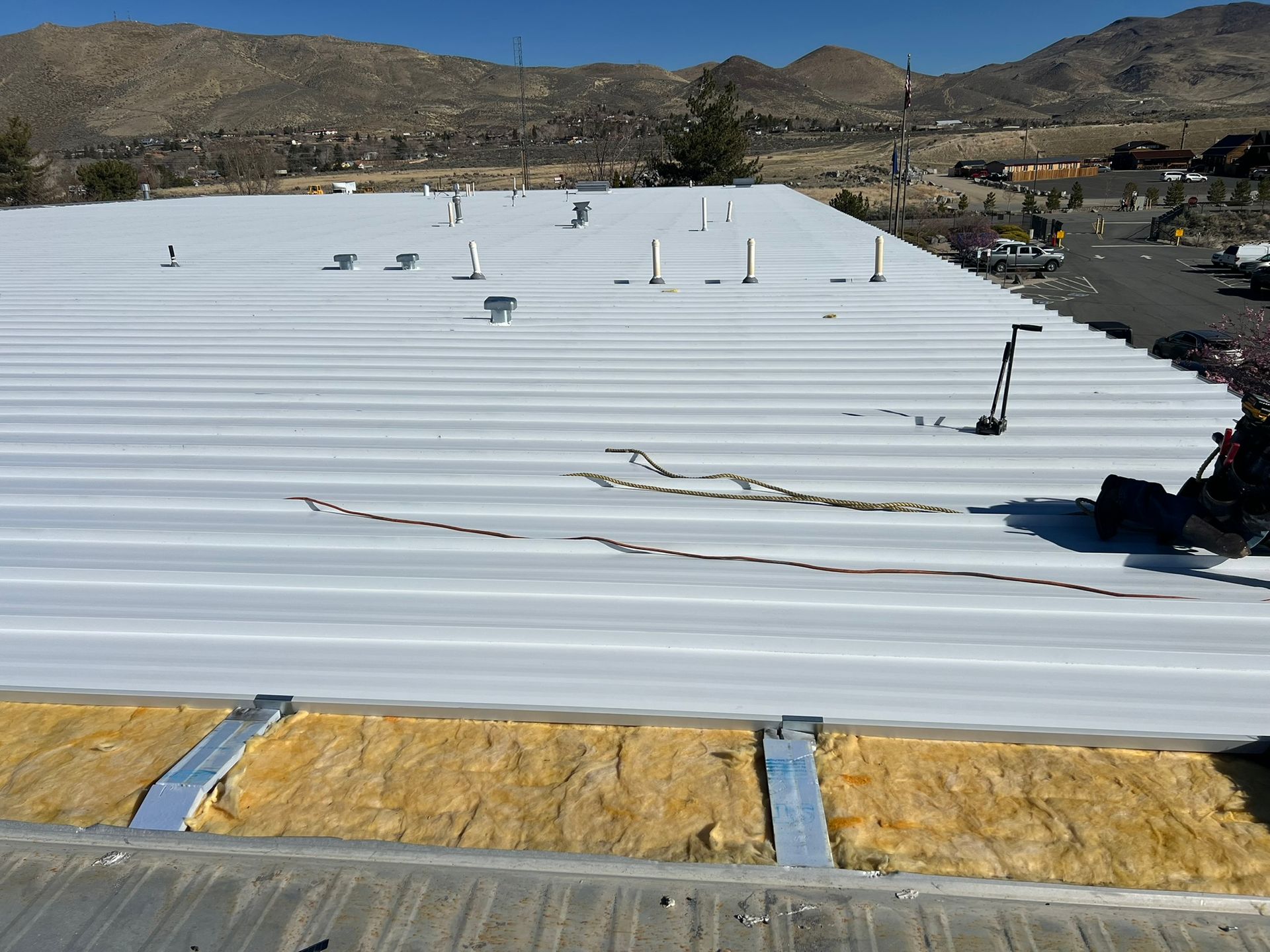 White corrugated metal roof with insulation exposed at the edge, mountains in the background.