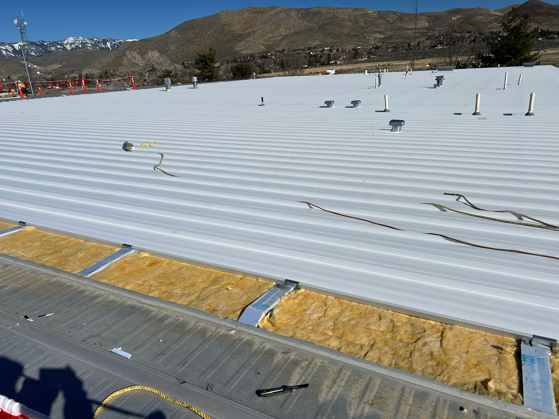 White roof with insulation exposed, construction site. Mountains in the background.