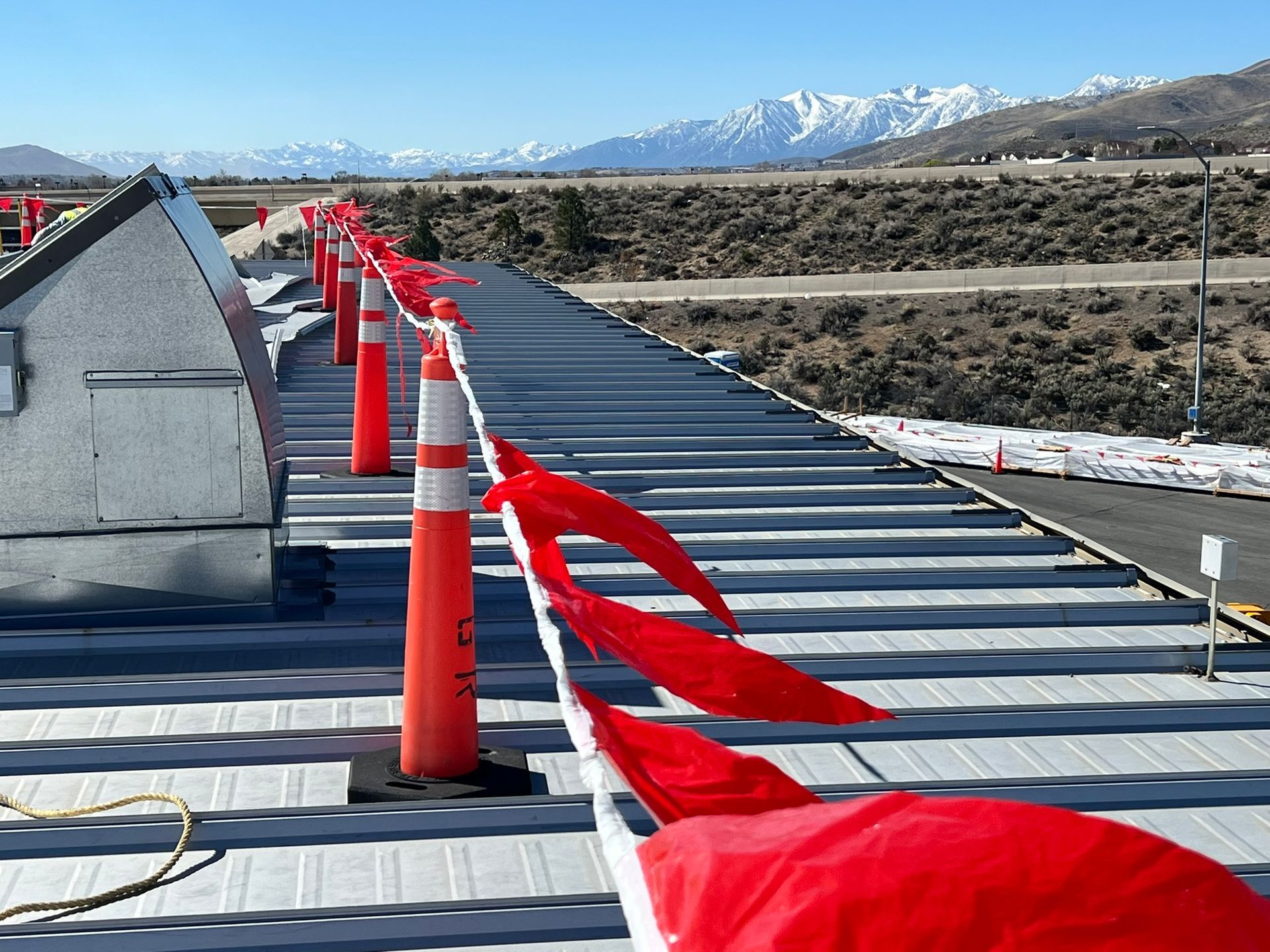 Orange traffic cones with red flags line a metal roof, mountains in the background.