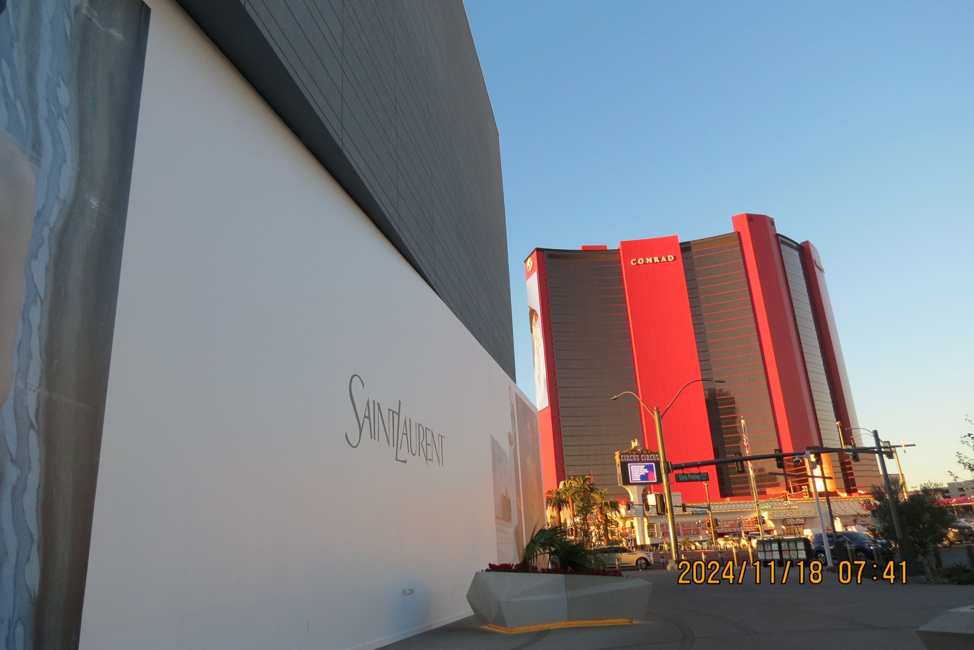 A modern building with a white facade and a red-and-black high-rise building on a sunny day.