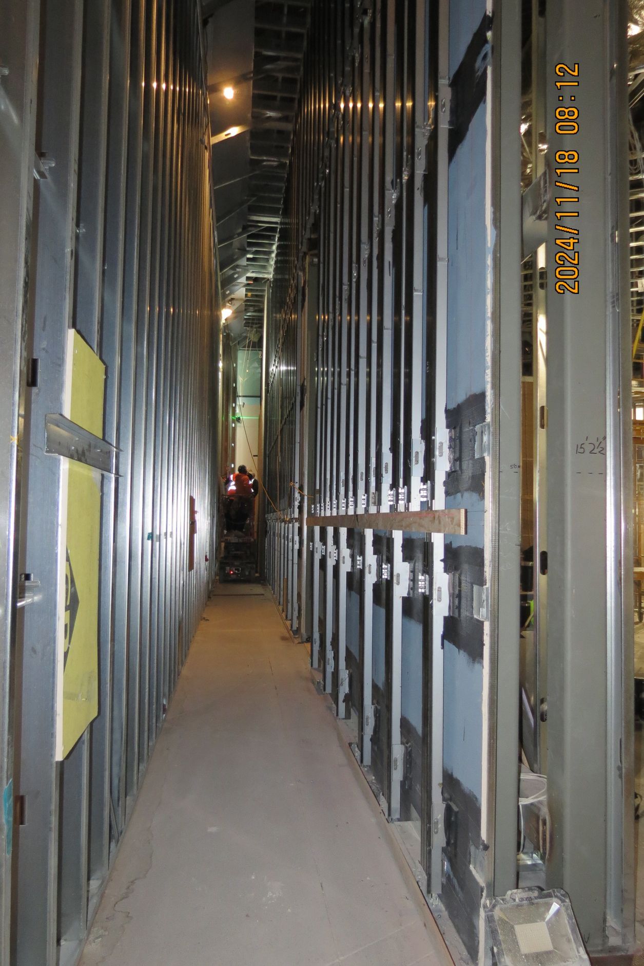 Narrow construction hallway with metal studs, insulation, and unfinished surfaces.