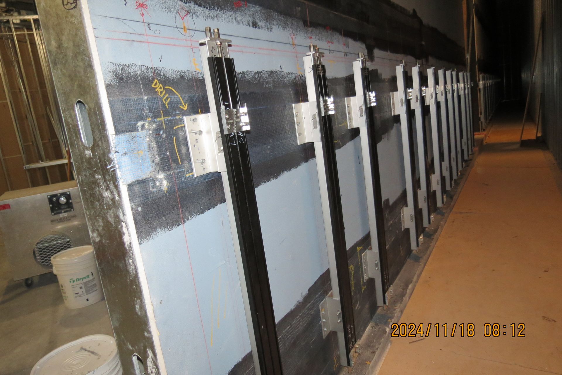 Wall with multiple dark, vertical panels and metal supports in a dimly lit industrial space.
