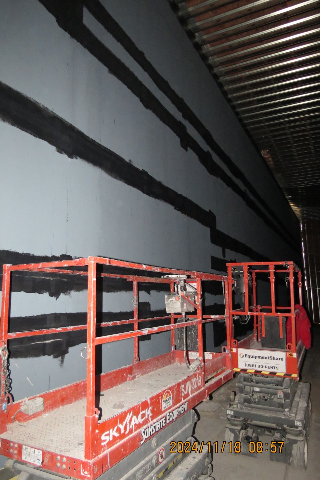 A scissor lift near a gray wall with black markings, possibly construction or repair.