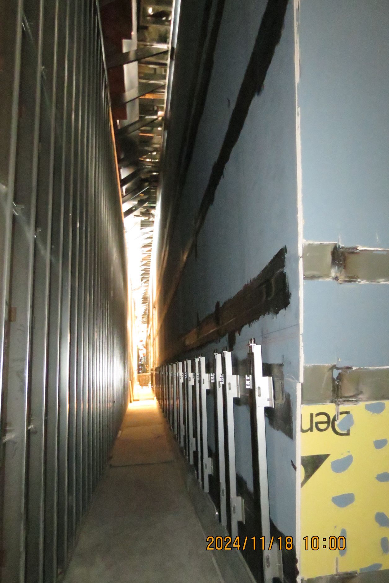 Narrow, metal-walled hallway with support structures on right wall.