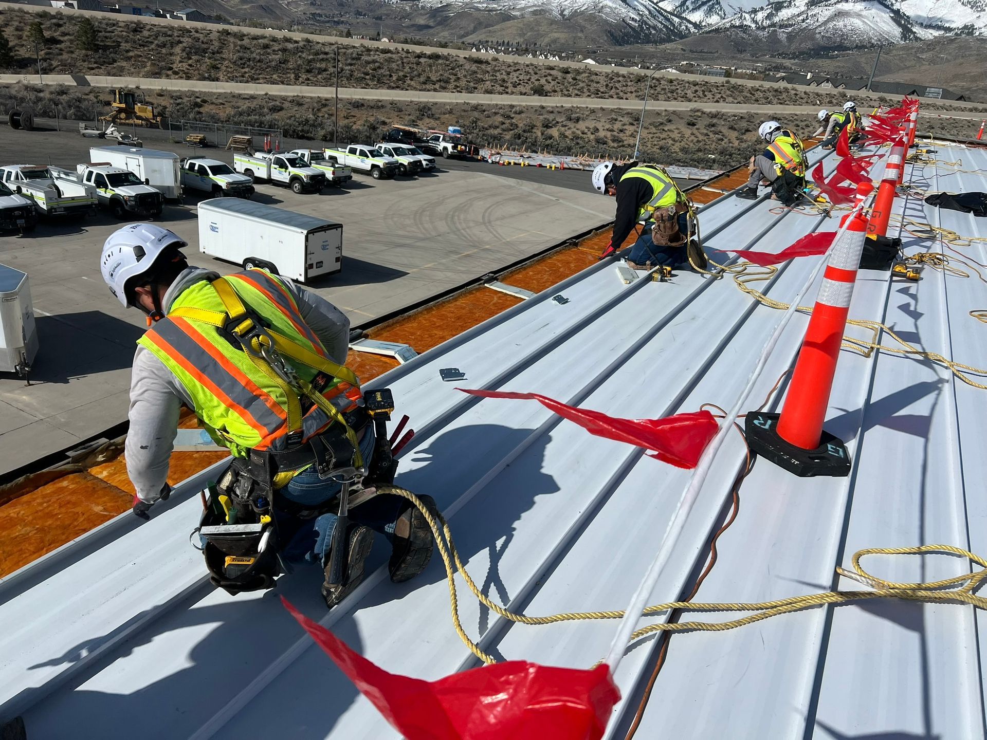 Construction workers on a white metal roof wearing safety gear