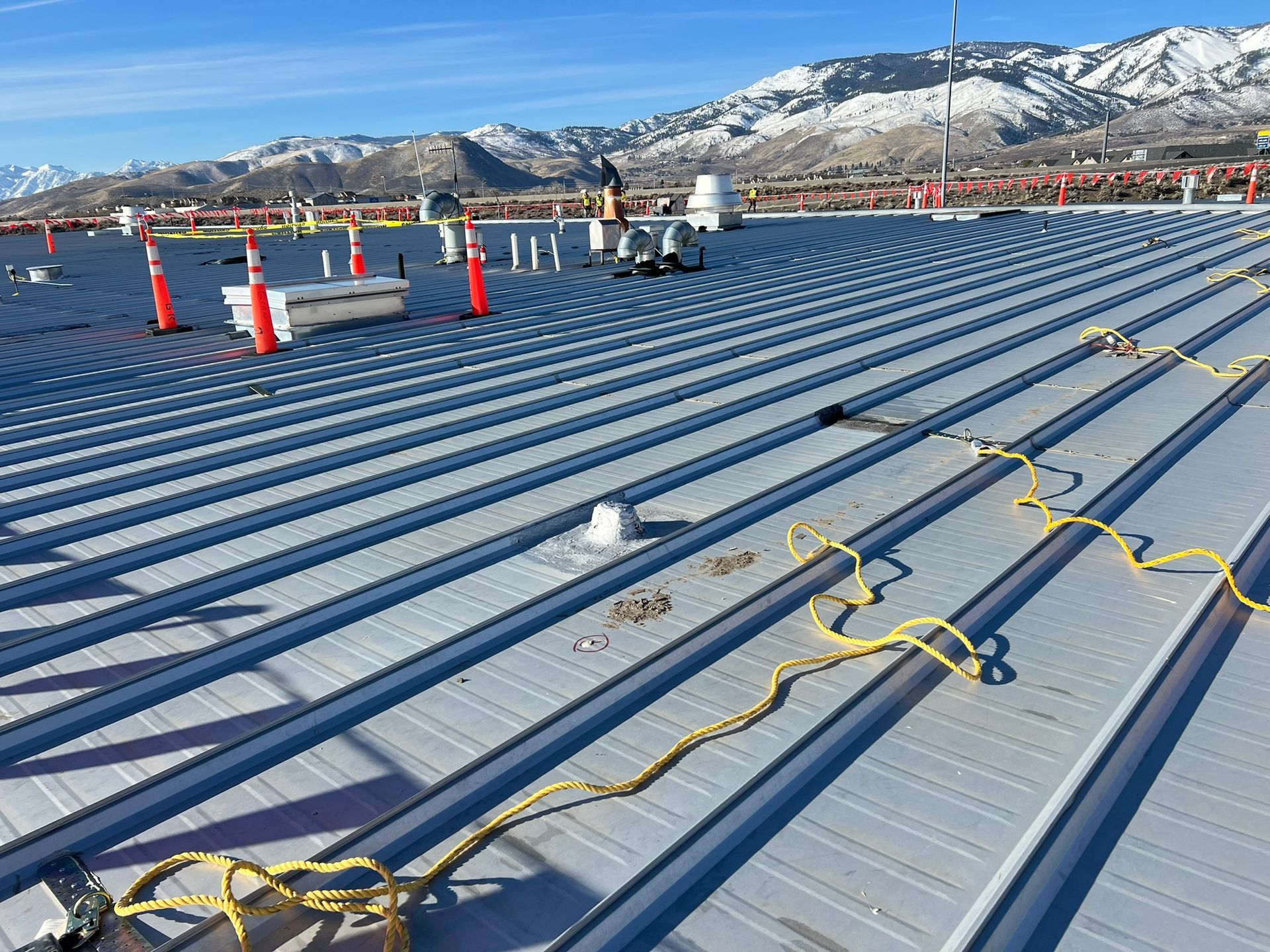 Metal roof with power cords and safety cones, snow-covered mountains in background.