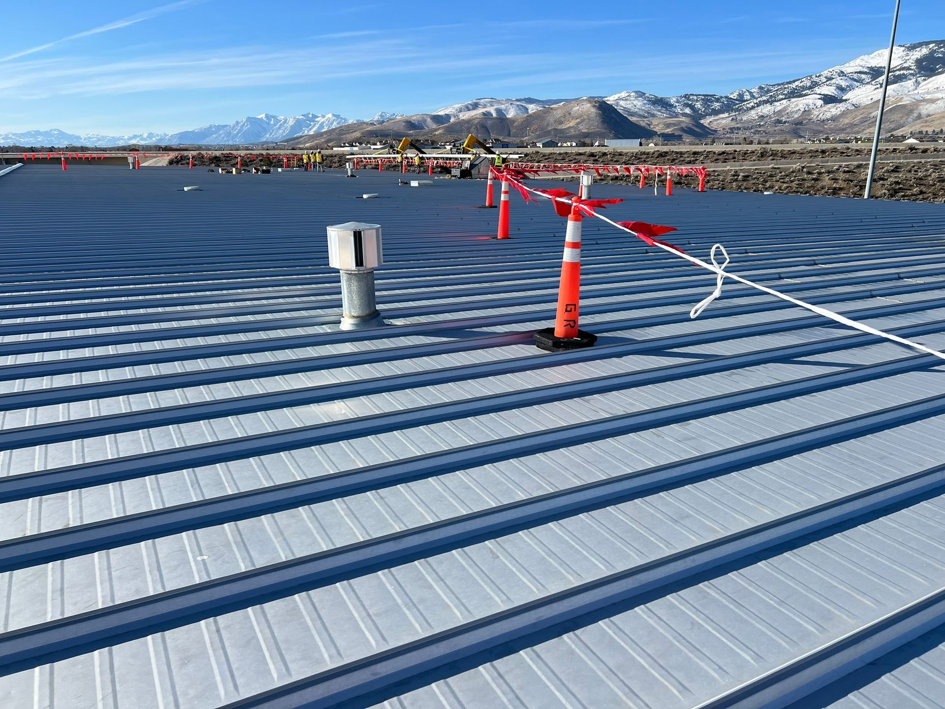 Metal roof with safety line and orange cones, mountains in background.