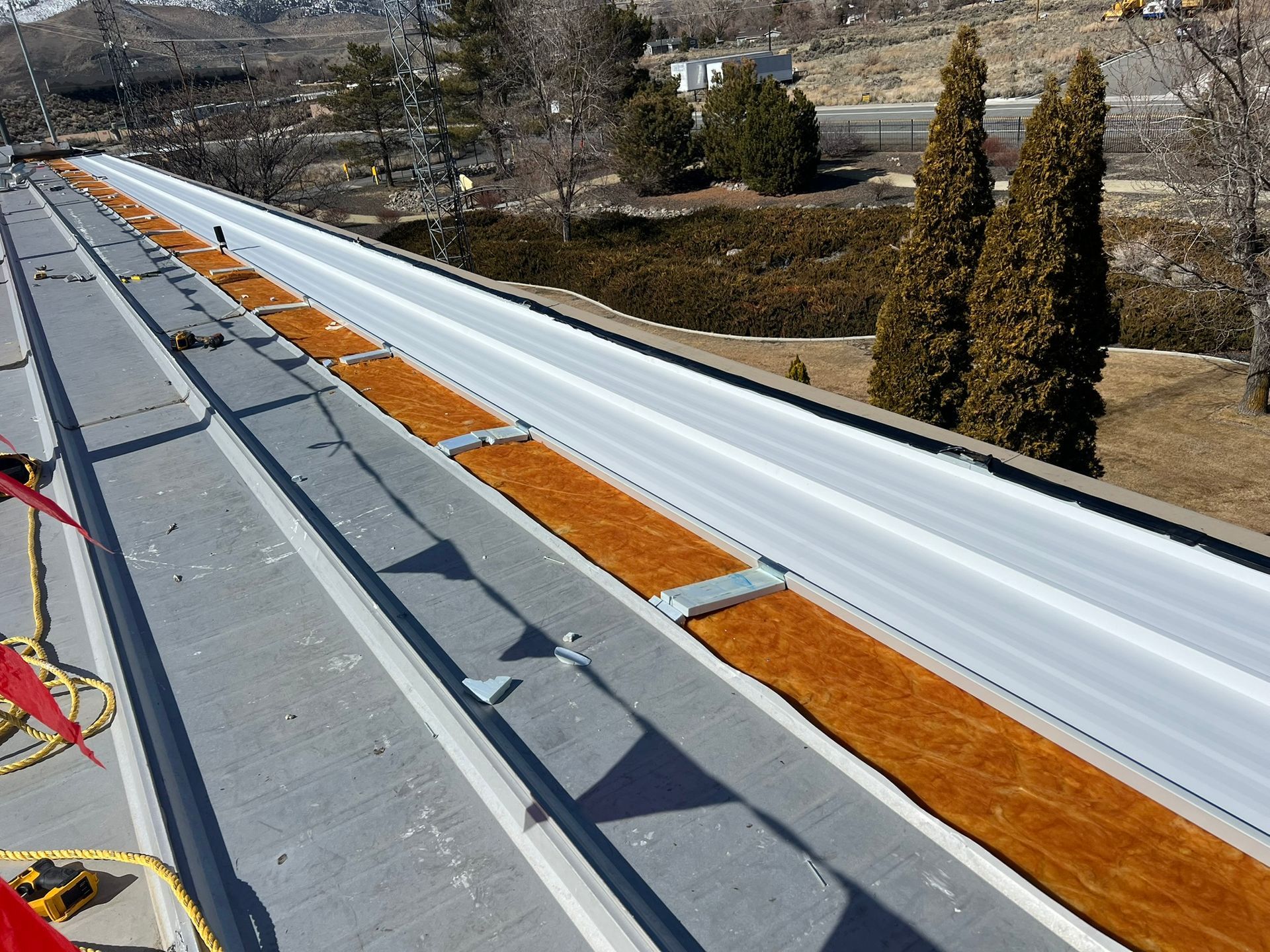 A metal roof with brown material installed in the valley. The background shows trees and a building.