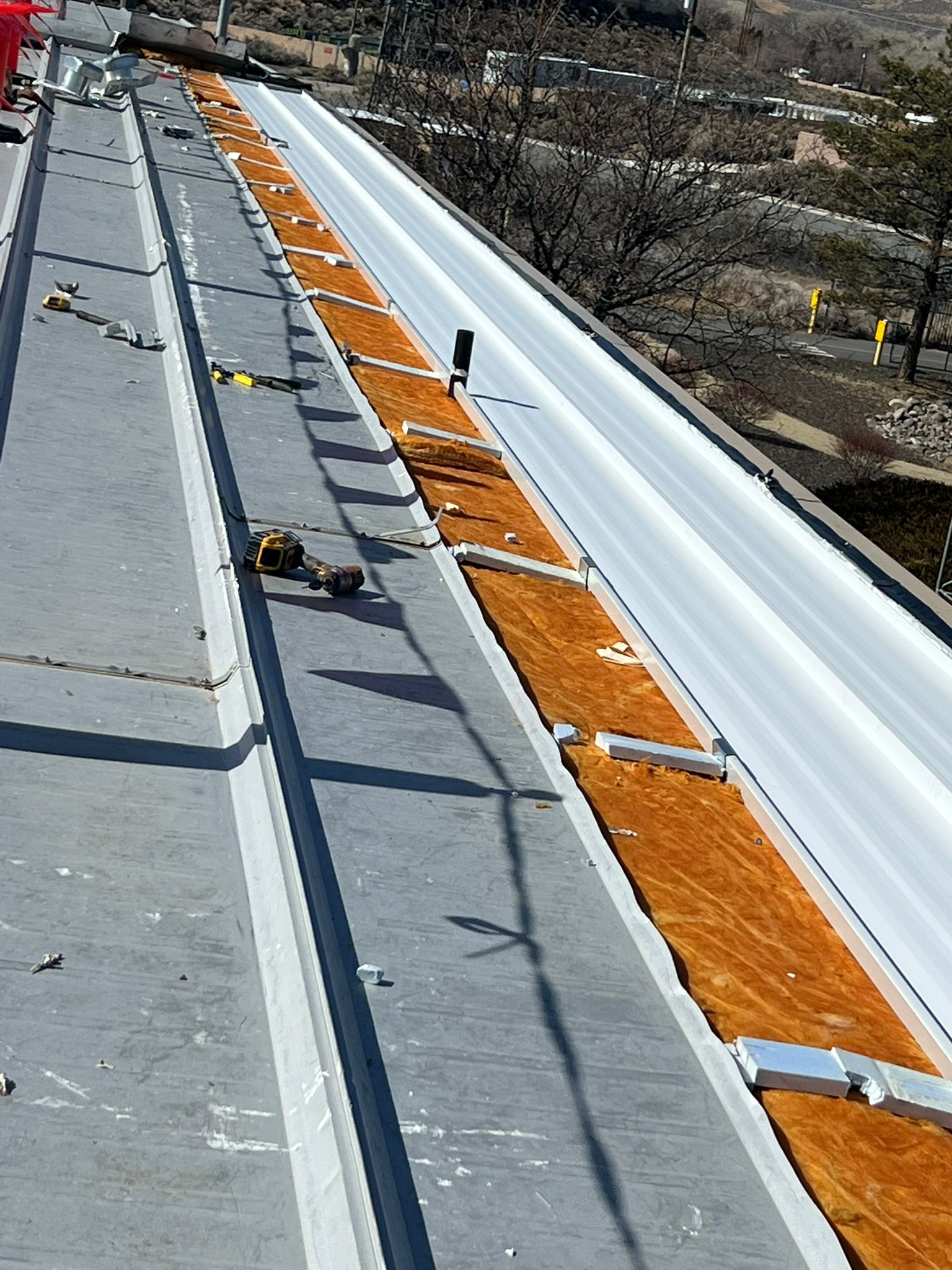 Overhead view of a long, gray industrial rooftop with a center white surface and a strip of orange material.