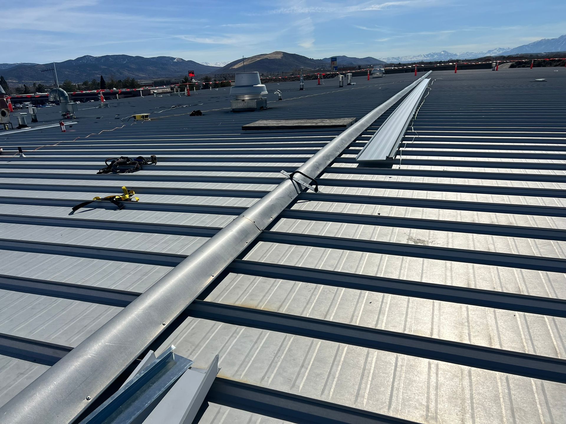 Metal roof with a long, silver rail system installed, with a background of mountains and a clear sky.