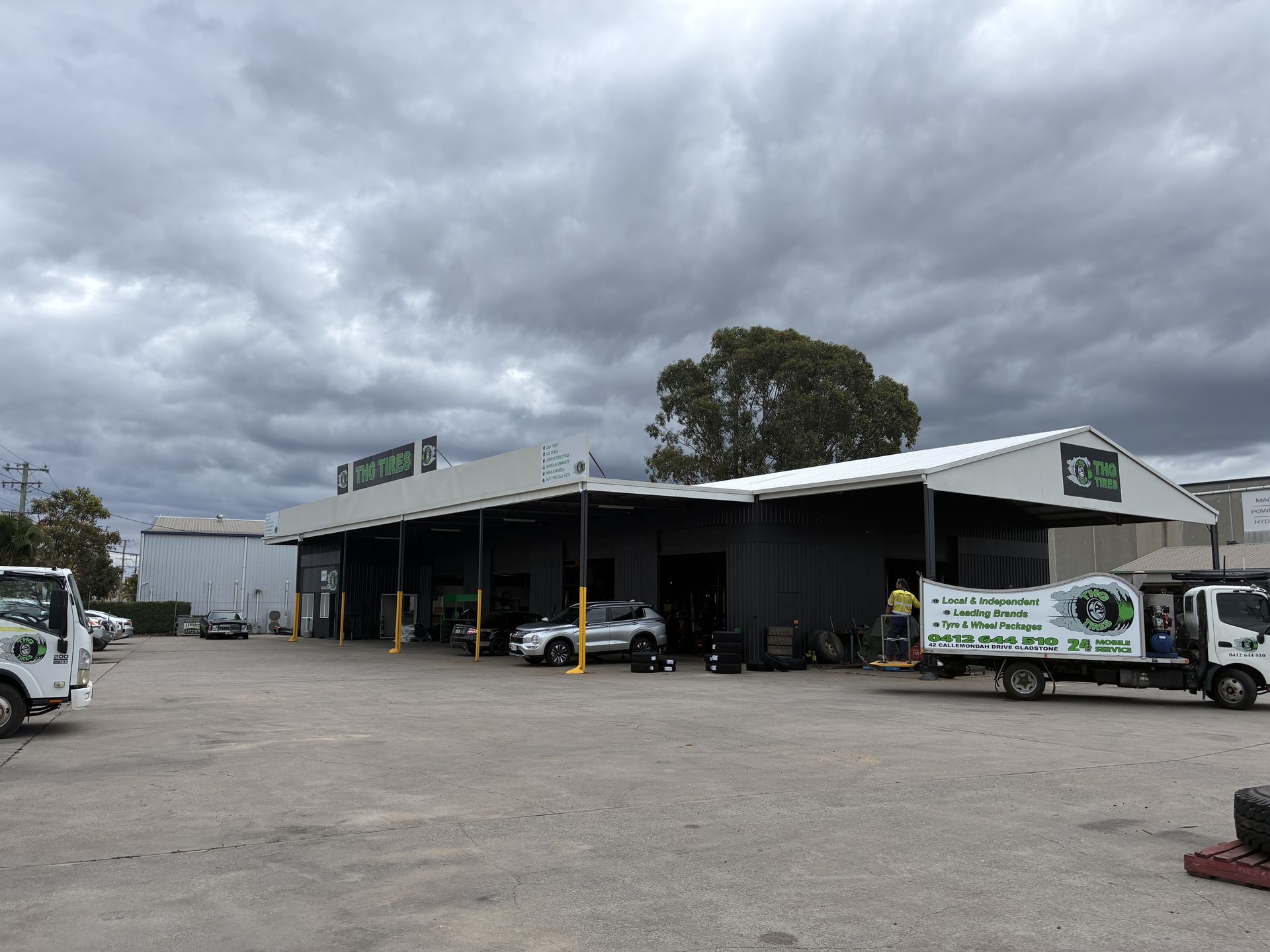 Industrial warehouse yard with parked vehicles under a cloudy sky - THG TIRES