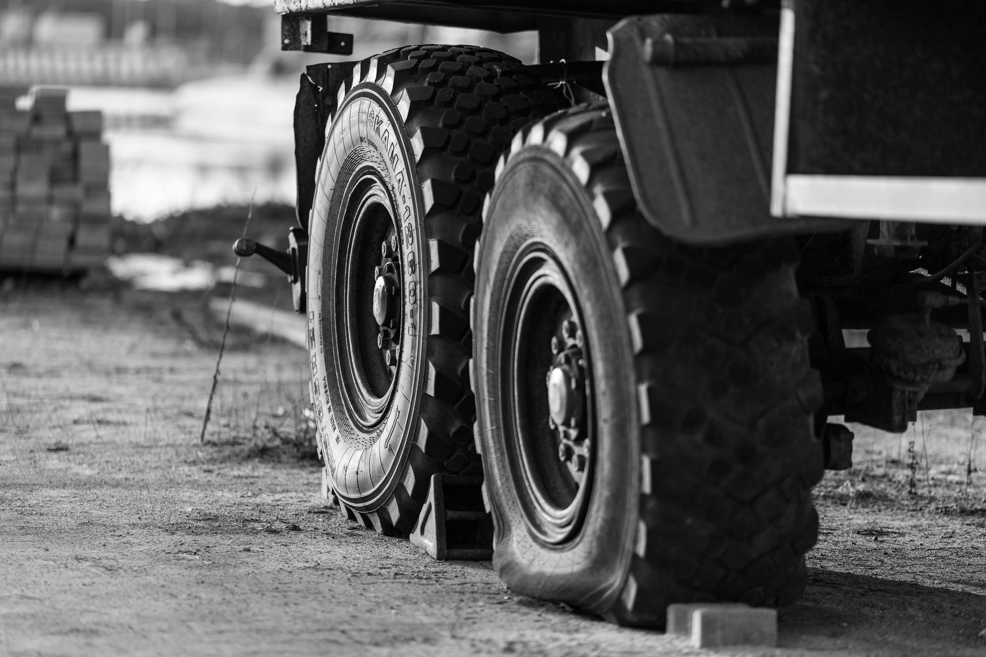 A Person In A Blue Vest And Cap Crouches Beside A Teal Semi-truck — THG Tires in Gladstone Central, QLD