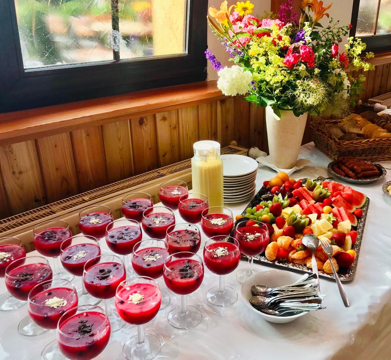 Ein Buffettisch mit einer Obstplatte und Blumen, neben einem Fenster mit Holzverkleidung.