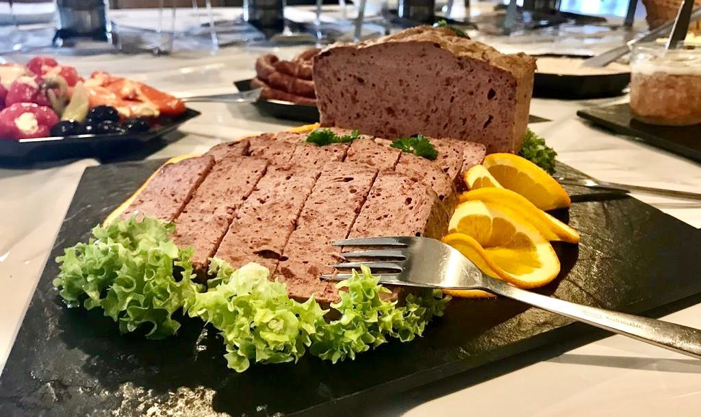 Aufgeschnittene Pastete mit Orangenscheiben und Salat auf einem schwarzen Servierbrett; weitere Speisen sind auf dem Tisch zu sehen.