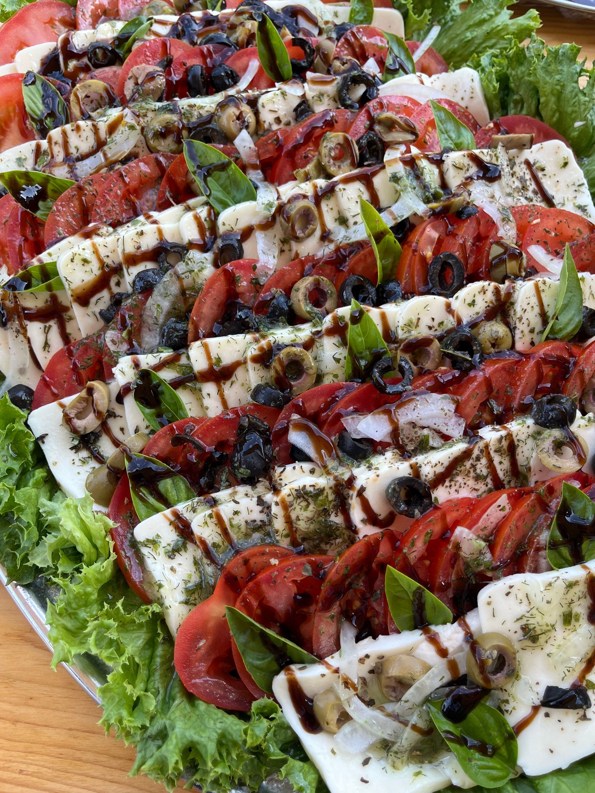 Caprese-Salatplatte: Tomaten, Mozzarella, gegrillte Paprika, Oliven, Basilikum und Balsamico-Glasur auf einem Salatbett.