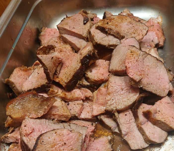 In Scheiben geschnittenes Roastbeef in einer Metallschale, innen rosa und außen gebräunt.