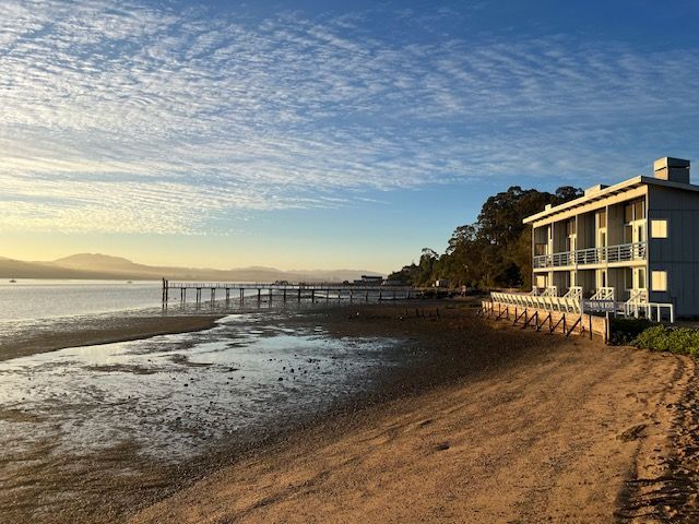 A house is sitting on a sandy beach next to a body of water.