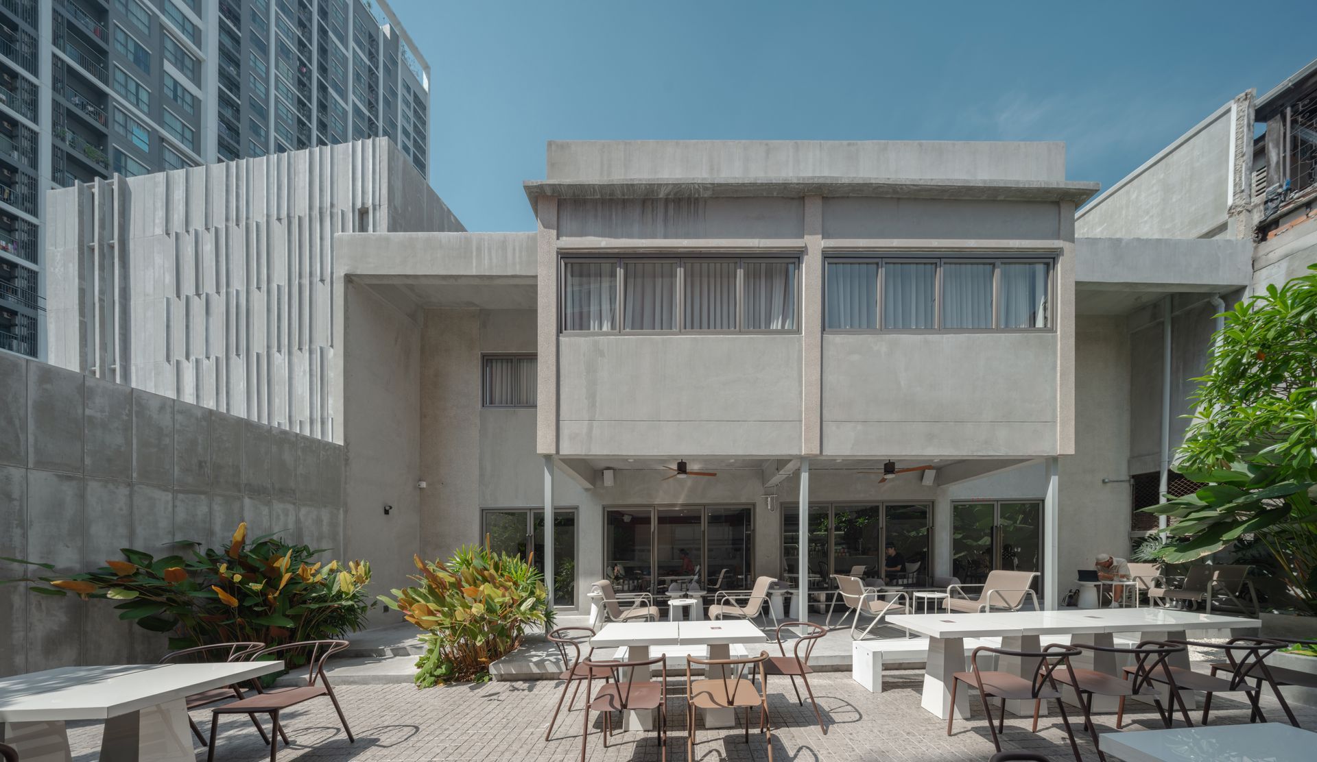 Modern concrete courtyard with outdoor café tables, chairs, and surrounding glass office buildings
