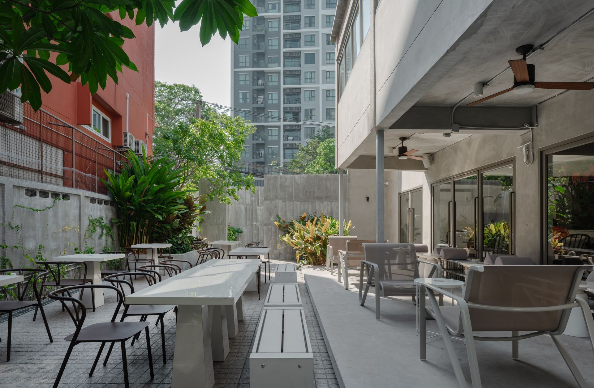 Outdoor café patio with metal tables and chairs beside a building, framed by trees and city apartments