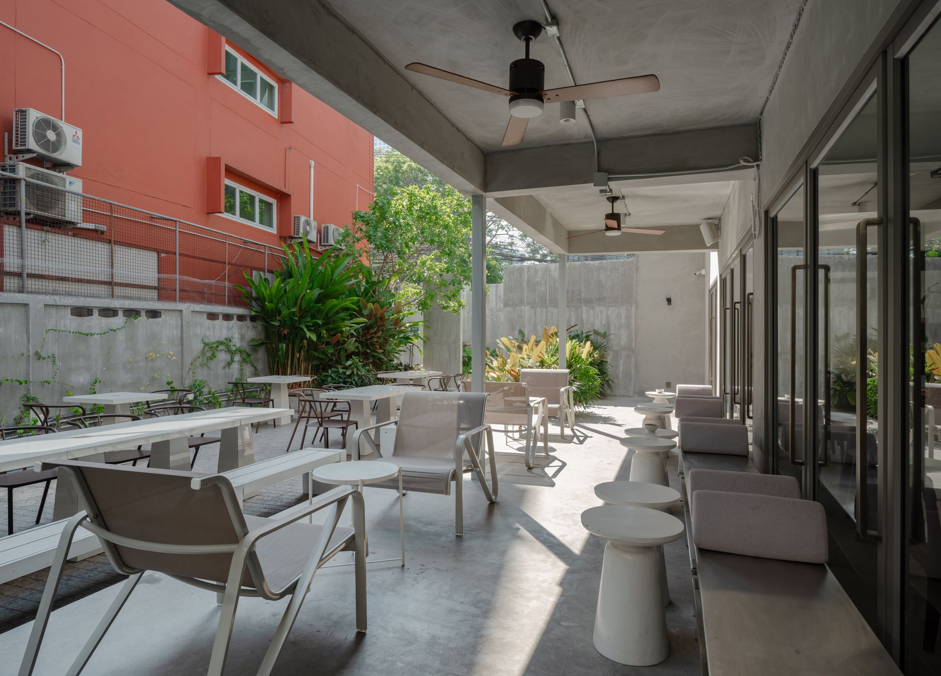 Outdoor patio with white tables and chairs beside a glass-walled building and red apartment block