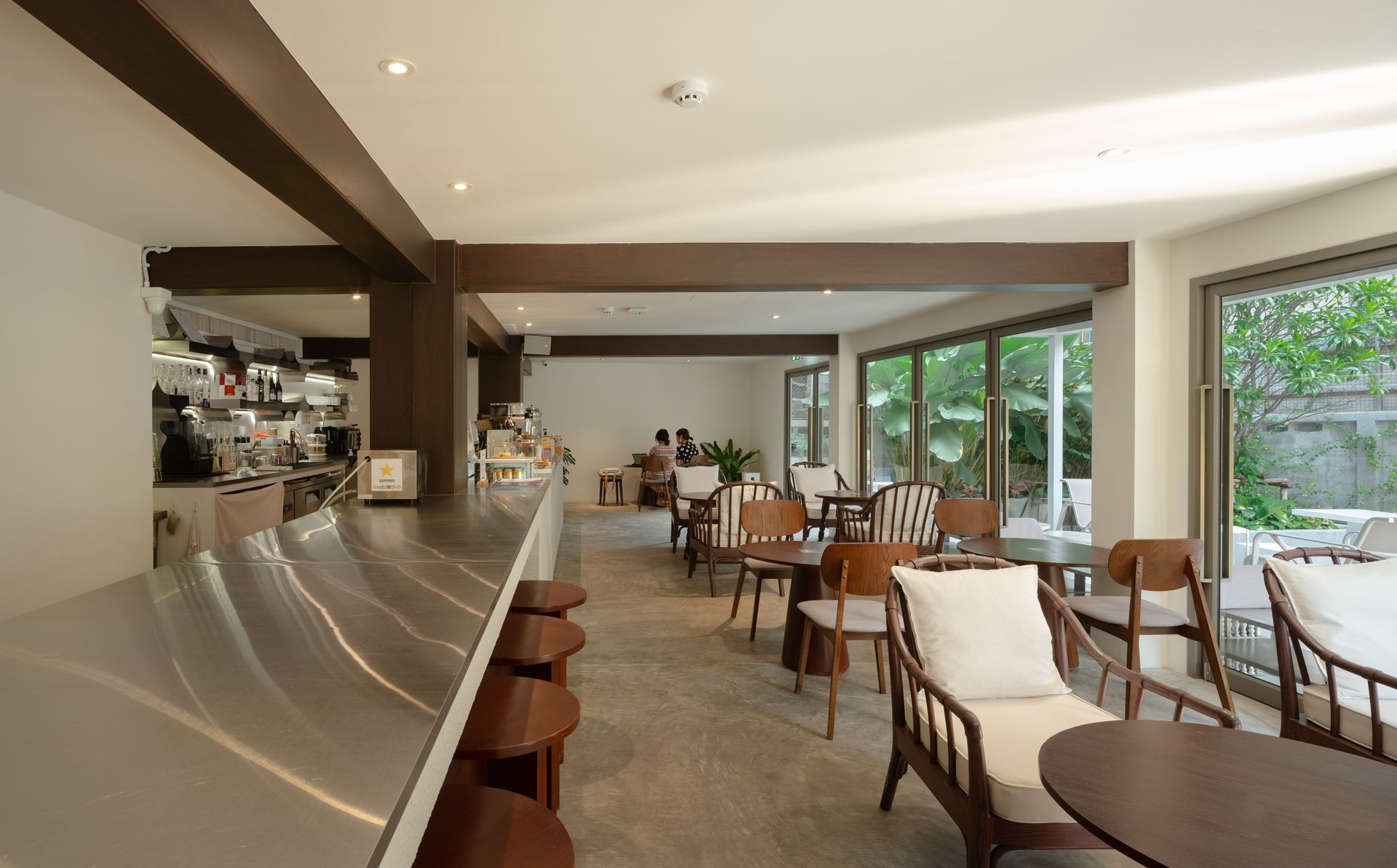 Bright café interior with long counter, tables, chairs, and large windows overlooking greenery