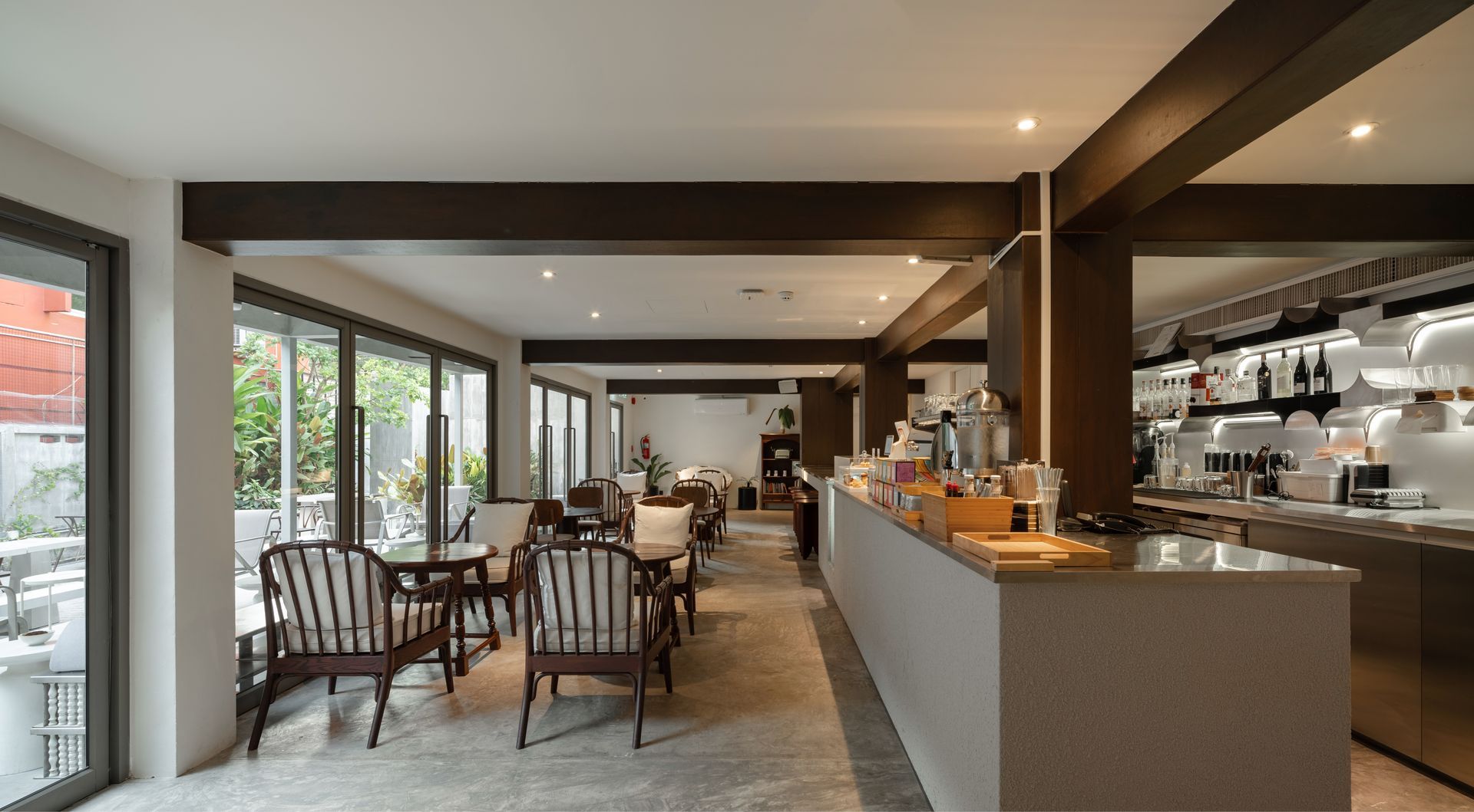 Modern restaurant interior with wooden tables, bar counter, and large windows letting in natural light