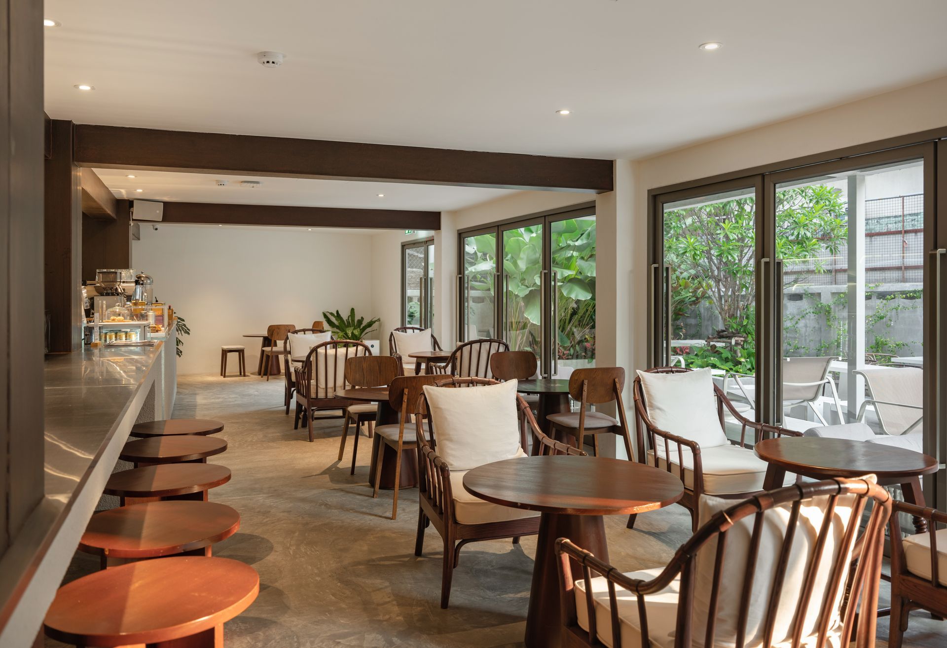 Modern café interior with wooden tables and chairs, large windows, and an empty counter seating area.